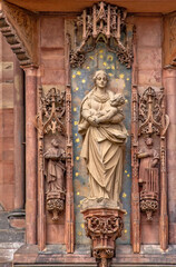 Fototapeta premium Detailed view of a Madonna and Child statue surrounded by ornate Gothic carvings and religious figures on the facade of Strasbourg Cathedral in France.