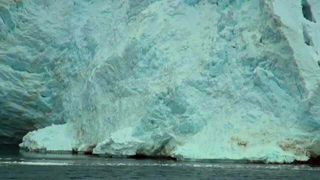 Massive turquoise walls of ice break away and collapse into the chilling ocean depths of Antarctica during a sunny afternoon trip.