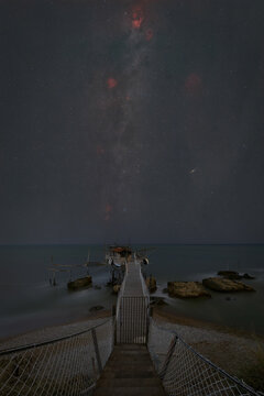 View of Trabocco Punta Torre at night under a starry sky with the Milky Way visible above the wooden structure and calm sea in Piane Favaro III, Provincia di Chieti, Italy.