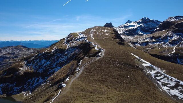 Luftaufnahme &uuml;ber geschwungenen Berggrat mit Schneeresten &ndash; Blick auf versteckten Bergsee in gr&uuml;ner Mulde