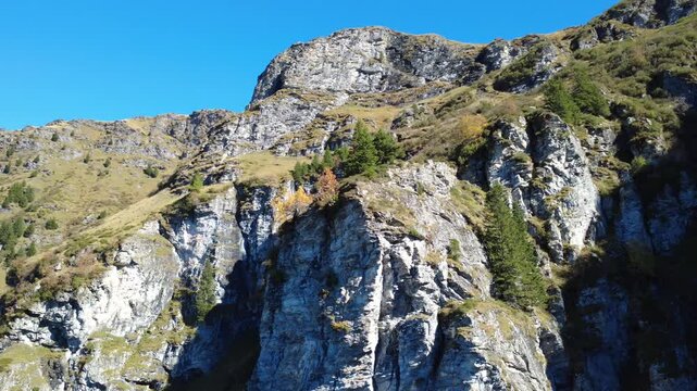 Felswand mit Wasserfall und herbstlich gef&auml;rbten B&auml;umen &ndash; Farbkontrast vor weitem Bergpanorama