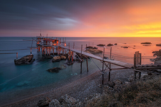 View of the traditional Trabocco Punta Torre fishing structure over the Adriatic Sea at sunset, with a wooden walkway and rocky coastline in Piane Favaro III, Provincia di Chieti, Italy.