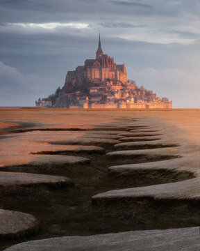 View of the historic abbey rising above the tidal flats during the golden hour in Mont Saint-Michel, Normandy, France.