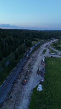 Vertical screen aerial drone view of two commuter trains passing each other on parallel railway tracks creating a dynamic transportation scene surrounded by green landscape