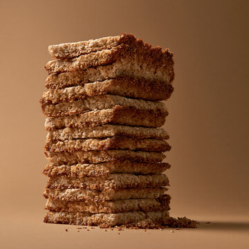 Tall stack of crispy golden brown oat biscuits on a solid light brown