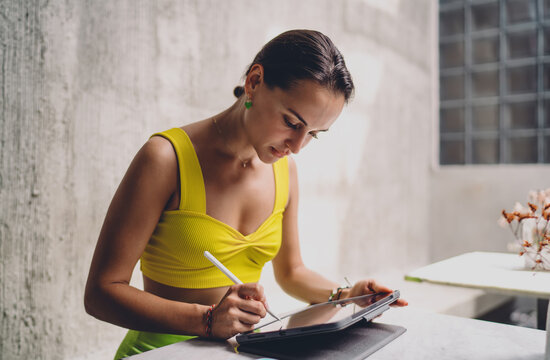 Digital art creator sketching illustration on tablet with stylus, focused Caucasian female designer working inside modern coworking cafe, hybrid lifestyle career autonomy copy space.