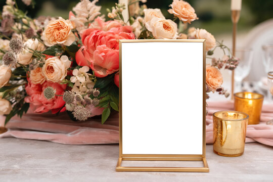 Blank gold table sign surrounded by peach flowers and candles at an elegant wedding reception