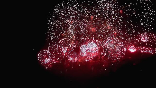 Vibrant firework displays light up the night sky. Explosions of red and white illuminate the darkness during an outdoor Fourth of July festival.