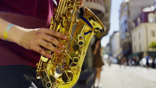 Male fingers of musician play the saxophone on summer day. Natural light reflects off metal surface, highlighting movement and rhythm. Scene captures live urban music and atmosphere street performance