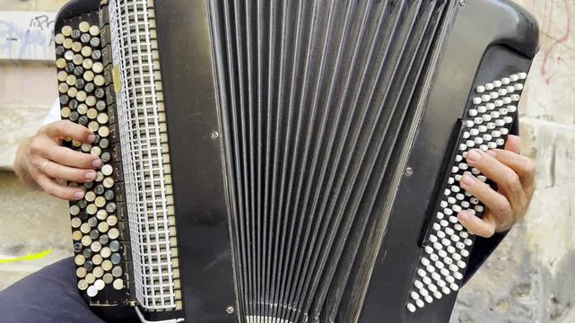 Male hands of musician playing the accordion at urban street. The detailed view highlights texture of instrument, capturing rhythm, tradition, and the expressive character of live music performance