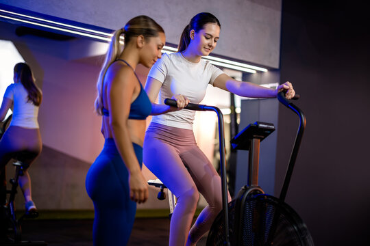 Full-length side profile of a fit woman in sportswear preparing to use or standing next to an indoor rowing ergometer.