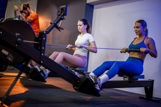 Side view of a fit woman sitting and using a resistance band or cable pulley machine for arm and back exercises.