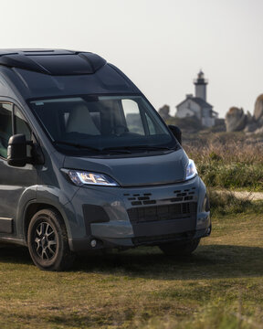 View of a grey camper van parked on a grassy field with the historic Pontusval lighthouse in the background in Plouneour-Brignogan-plages, Bretagne, France.