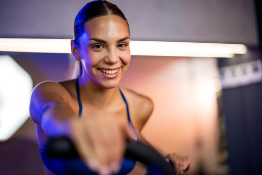 Close-up portrait of a beautiful, happy young woman smiling directly at the camera while taking a break in a fitness center.