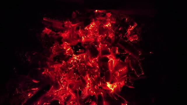 Close up of glowing charcoal embers burning with red and orange tones at night. Soft heat and shimmering texture create magical atmosphere. Warm abstract scene symbolizing warmth and quiet at nature