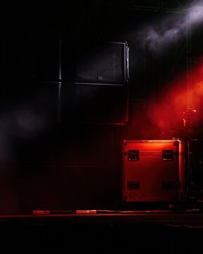 Line array speaker system suspended over a stage with a red flight case, featuring gritty textures and atmospheric smoke for concert production