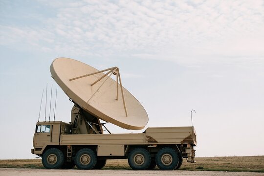 Large parabolic antenna on a heavy truck chassis, featuring a weathered matte finish and textured mesh for communications infrastructure and defense technology, with copy space
