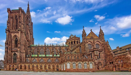 Fototapeta premium Wide view of Strasbourg Cathedral showing its Gothic facade, monumental tower, ornate tracery, stained glass windows, sandstone walls and green copper roofs in Strasbourg, France.
