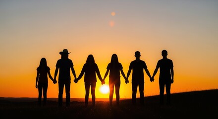 Fototapeta premium Six people stand hand in hand on a hill, silhouetted against a golden sunset. The warm orange sky creates an inspiring scene of unity, teamwork, friendship, and togetherness.