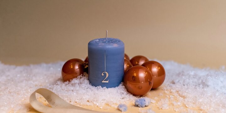 Blue advent candle with numeral two on fresh snow, featuring glossy ornaments and a soft glow for holiday catalogs and winter greeting cards