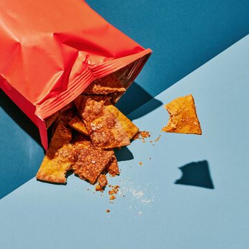 Red foil snack pouch with baked pita triangles spilling out, featuring salt grains and blistered textures for a product mockup and packaging layout