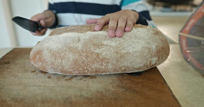 Kid hands cut bread with knife. Boy help in kitchen. 4K 10-bit