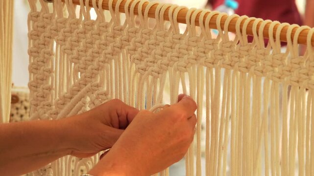 Woman weaving a macrame loom with white rope.