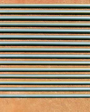 Galvanized pipework in parallel rows, featuring oxidized weld beads and metallic spangle on compacted soil for industrial design patterns