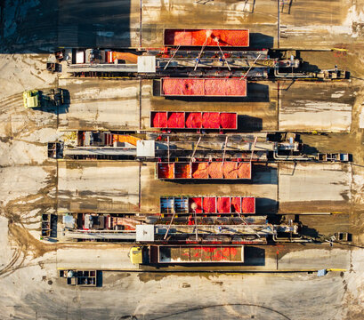 Aerial view of a tomato processing facility with trucks unloading fresh red tomatoes into industrial sorting machinery at a food factory in Pomposa, Emilia-Romagna, Italy.