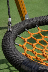 Close up of bird nest swing with orange net and black rope rim on outdoor playground for summer childhood concept © Marina
