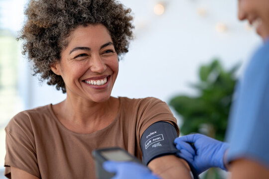 Black woman smiles while a healthcare professional measures her blood pressure. Health screening, patient care, medical checkup.