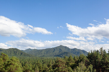 Fototapeta premium Lush green mountains rise under a bright blue sky with scattered clouds, creating a serene and picturesque natural landscape