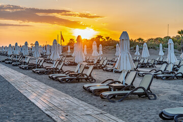 Fototapeta premium Backlit beach chairs and umbrellas beneath a glowing Mediterranean sunset in Antalya, Turkey.