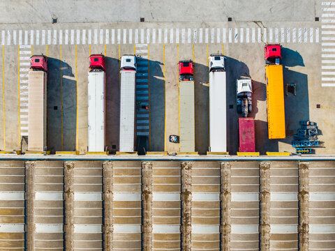 Aerial view of semi-trucks parked at the loading bays of a food factory with colorful trailers and concrete pavement in Pomposa, Emilia-Romagna, Italy.