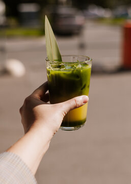 Close up of iced green matcha tea. Creative trendy healthy drink background concept. Matcha texture backdrop idea with ice, matcha bumble with orange juice. Flat lay style. Top view banner