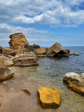A high-angle, close-up shot of weathered limestone rocks and boulders on a serene sea shore