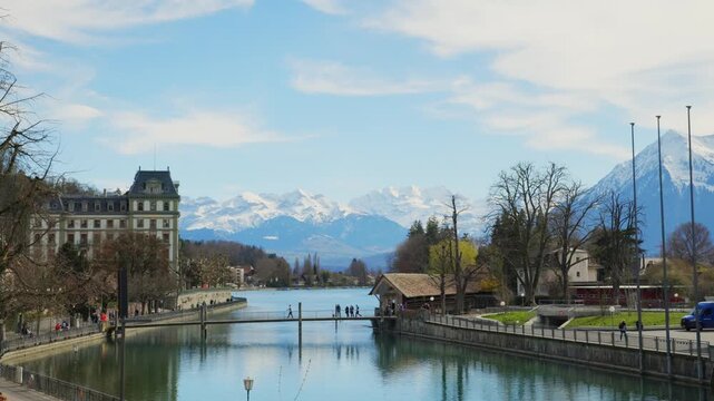 Static view of pedestrians on bridge in Thun with snow capped Alps background