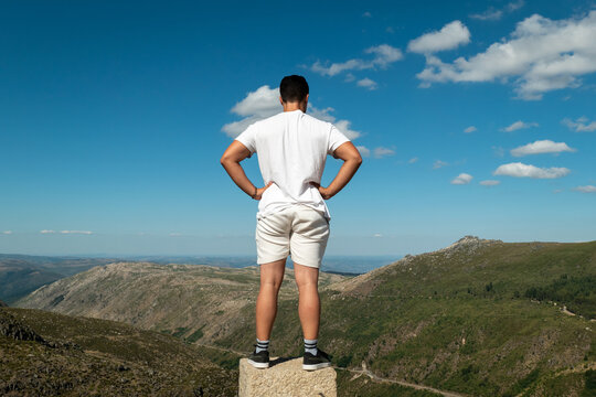 Jovem turista no topo de um rochedo a contemplar a vista panor&acirc;mica sobre as montanhas da Serra da Estrela num dia ensolarado em Portugal
