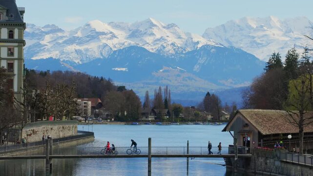 Static view of pedestrians on bridge in Thun with snow capped Alps background