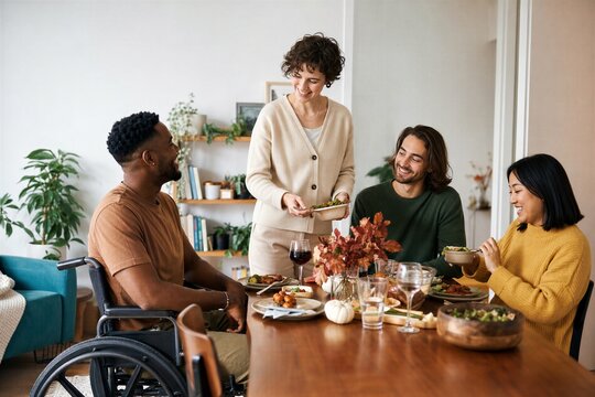 Diverse group of friend eating healthy dinner at home. Young woman serving food to african american man in wheelchair and multiethnic friends.