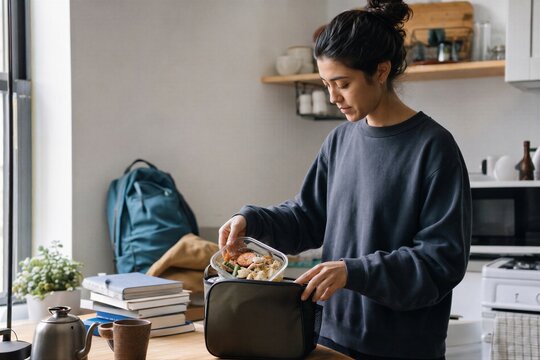 Woman packing healthy meal in reusable glass container into lunch bag. Sustainable lifestyle and low waste food storage in kitchen.