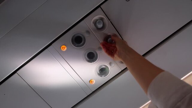 Close up of passenger hand reaching up to adjust reading light or air vent nozzle on airplane overhead console inside cabin.