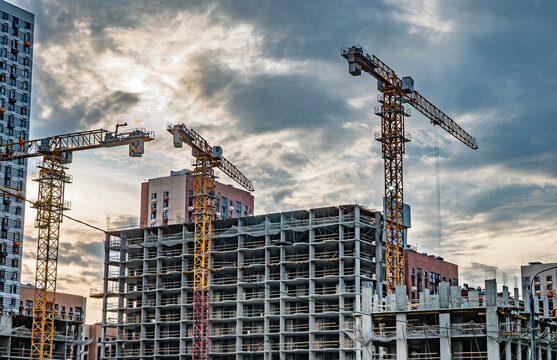 Tower cranes working on modern residential building construction site against dramatic cloudy sky