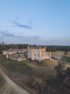 Aerial view of a historic chateau with stone walls and red shutters, surrounded by rolling vineyards and lush trees in the countryside of Puisseguin, Nouvelle-Aquitaine, France.
