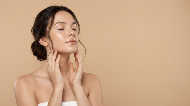 Woman with eyes closed wrapped in towel touching neck on tan background for spa skincare wellness