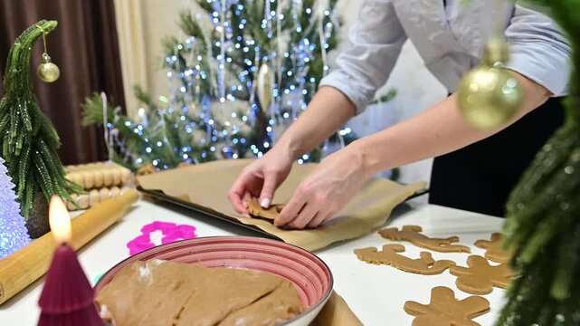 A woman works in the kitchen placing gingerbread horses on a baking sheet. The Christmas tree and garlands shine bright in the background creating a festive mood.