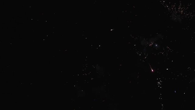 Spectacular fireworks explode across the night sky, sending bright colorful rockets and showers of glowing sparks upward through clouds of smoke. The dynamic display creates a festive atmosphere
