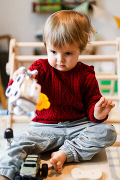 Cute Toddler Boy in Red Knit Sweater Playing with Toys at Home During Christmas Holidays. Family domestic moments