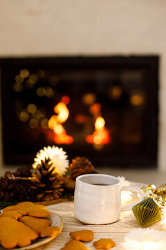 Warm cup of tea with gingerbread cookies on decorated table in front of glowing fireplace. Cozy xmas eve, happy holidays