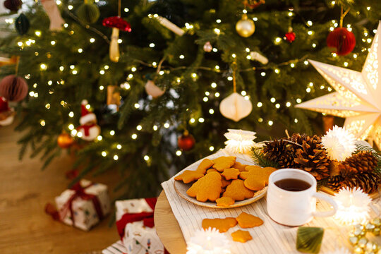 Warm Christmas Evening Still Life with Gingerbread Cookies, Coffee Mug, Pine Cones, and Illuminated Christmas Tree. Cozy xmas eve, winter holidays